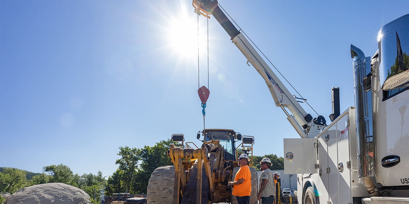 Two men in hard hats operating a 12621 crane to lift a large equipment.