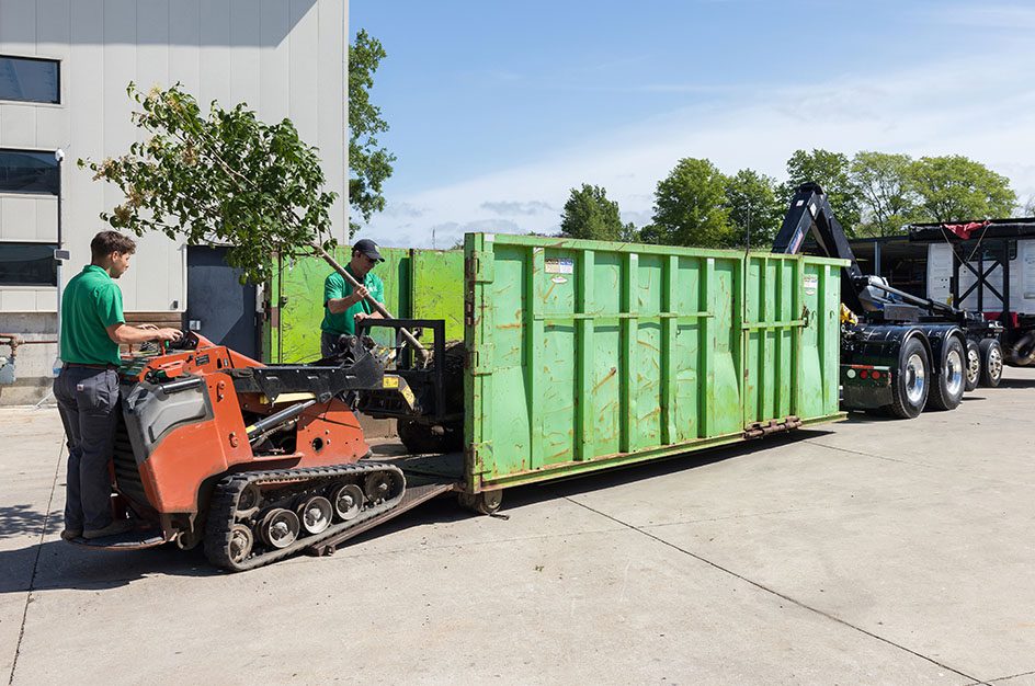 Two men loading small lift onto truck container
