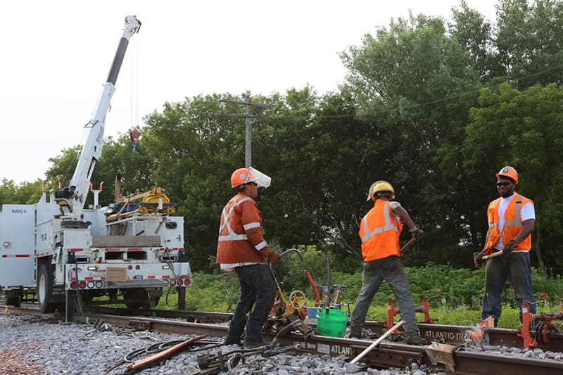 Three men in orange vest working on a rail road with a Stellar crane in the background