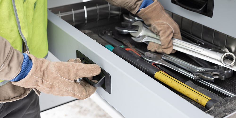 Person grabbing the bale-style pull handle from below while reaching into the drawer to pick up tools.